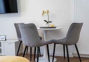Un comedor moderno con dos sillas grises, una mesa blanca y una orquídea en maceta.