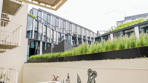 En modern byggnad med stora glasfönster, en takträdgård och ett vitt räcke.