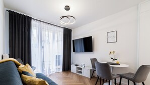 Ett modernt vardagsrum med en soffa, ett matbord, stolar, en platt-TV och ett litet vitt skåp.
