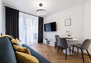 Una sala de estar moderna con un sofá, una mesa de comedor, sillas, un televisor de pantalla plana y un pequeño mueble blanco.