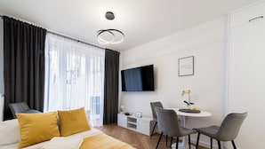 Ett hotellrum med en säng, ett skrivbord, två stolar, en tv och ett litet bord med blommor.
