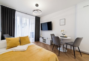 Une chambre d’hôtel avec un lit, un bureau, deux chaises, une télévision et une petite table agrémentée de fleurs.