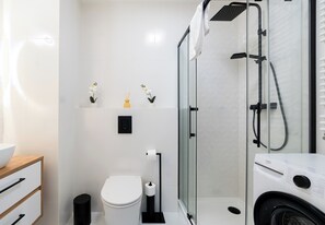 Un baño moderno con cabina de ducha de vidrio, inodoro, lavabo y lavadora.