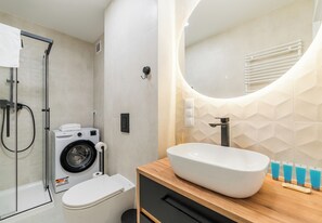 A bathroom with a washing machine, toilet, shower, and a large sink with a mirror. - Garbary Old Town Apartment #11 (Poznań)