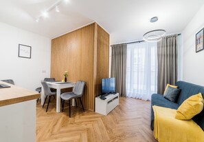 Un soggiorno moderno con una parete divisoria in legno, un'area pranzo, un divano con una coperta gialla e una TV su un mobile.