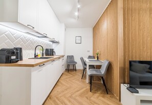 A modern kitchen with white cabinets, a wooden countertop, and a dining area with a table and chairs. - Garbary Old Town Apartment #11 (Poznań)