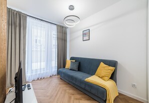 A modern living room with a sofa, a flat-screen TV, and a window with curtains. - Garbary Old Town Apartment #11 (Poznań)