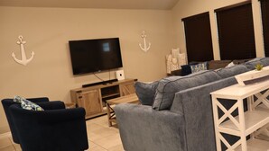 Ein Wohnzimmer mit Flachbildfernseher, grauem Sofa, blauem Sessel und weißem Konsolentisch.
