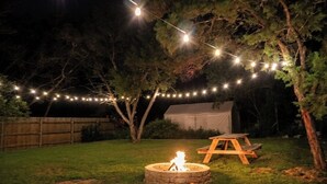 Ein Garten mit Feuerschale, einem Holztisch und Lichterketten.