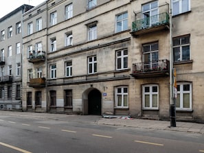 A multi-story building with balconies, a street in front, and a speed limit sign. - Łódź Homely Apartment (Łódź)