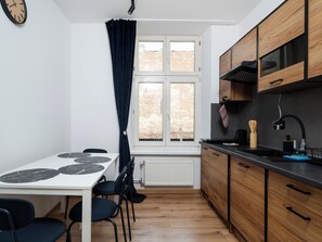 A compact kitchen with a dining table, chairs, wooden cabinets, a window with curtains, and a radiator. - Łódź Homely Apartment (Łódź)