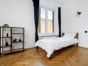 A bedroom with a wooden bed, a black metal shelf with plants, and a window with curtains. - Łódź Homely Apartment (Łódź)