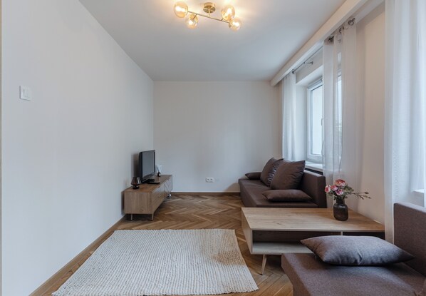 A modern living room with a sofa, a coffee table, a TV, and a herringbone floor pattern. - Jagiellońska Comfort Apartment (Rzeszów)