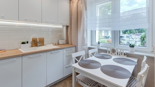 Een moderne keuken met witte kasten, een houten aanrecht, een spoelbak en een eethoek met een witte tafel en stoelen.