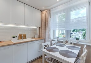 A modern kitchen with white cabinetry, a wooden countertop, a sink, and a dining area with a white table and chairs. - Jagiellońska Comfort Apartment (Rzeszów)