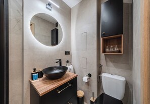 A modern bathroom with a wooden vanity, a round mirror, a black sink, and a toilet. - Jagiellońska Comfort Apartment (Rzeszów)