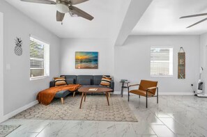 Een moderne woonkamer met een grijze bank, een salontafel, een stoel en een plafondventilator.