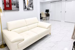 Een witte leren bank in een moderne kamer met een bureau, stoel en een witte kledingkast.