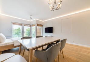 A modern room with a bed, a dining table with chairs, a TV, and large windows. - Warta River Chic Studio (Poznań)