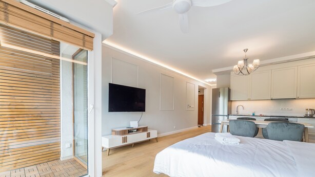 A modern hotel room with a large bed, a flat-screen TV, a dining area, and a kitchen. - Warta River Chic Studio (Poznań)