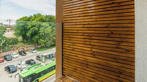A balcony with a wooden slat wall, a view of a street with cars and a bus, and a clear sky. - Warta River Chic Studio (Poznań)