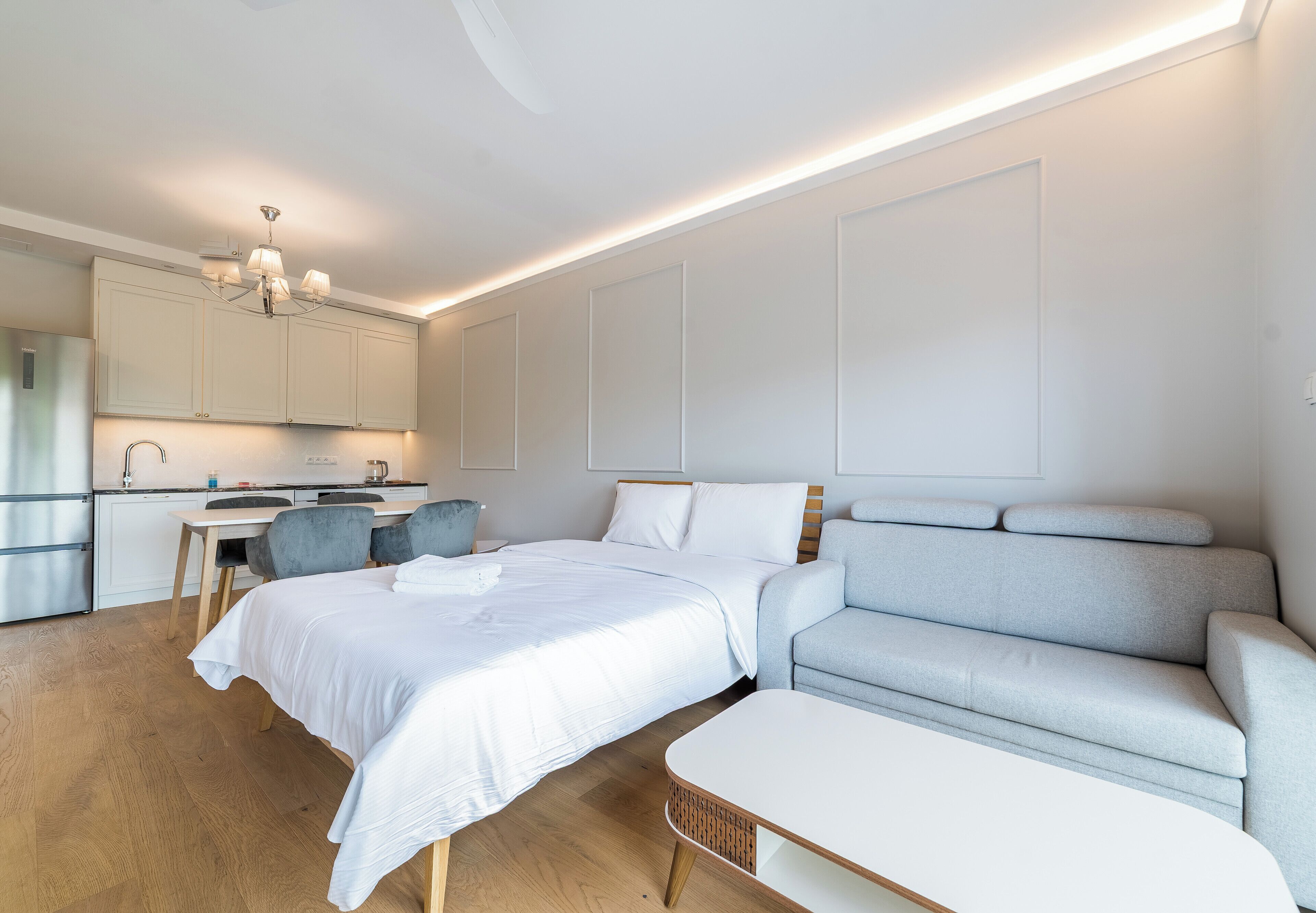 A modern bedroom with a bed, a sofa, a dining area, and a kitchen.
