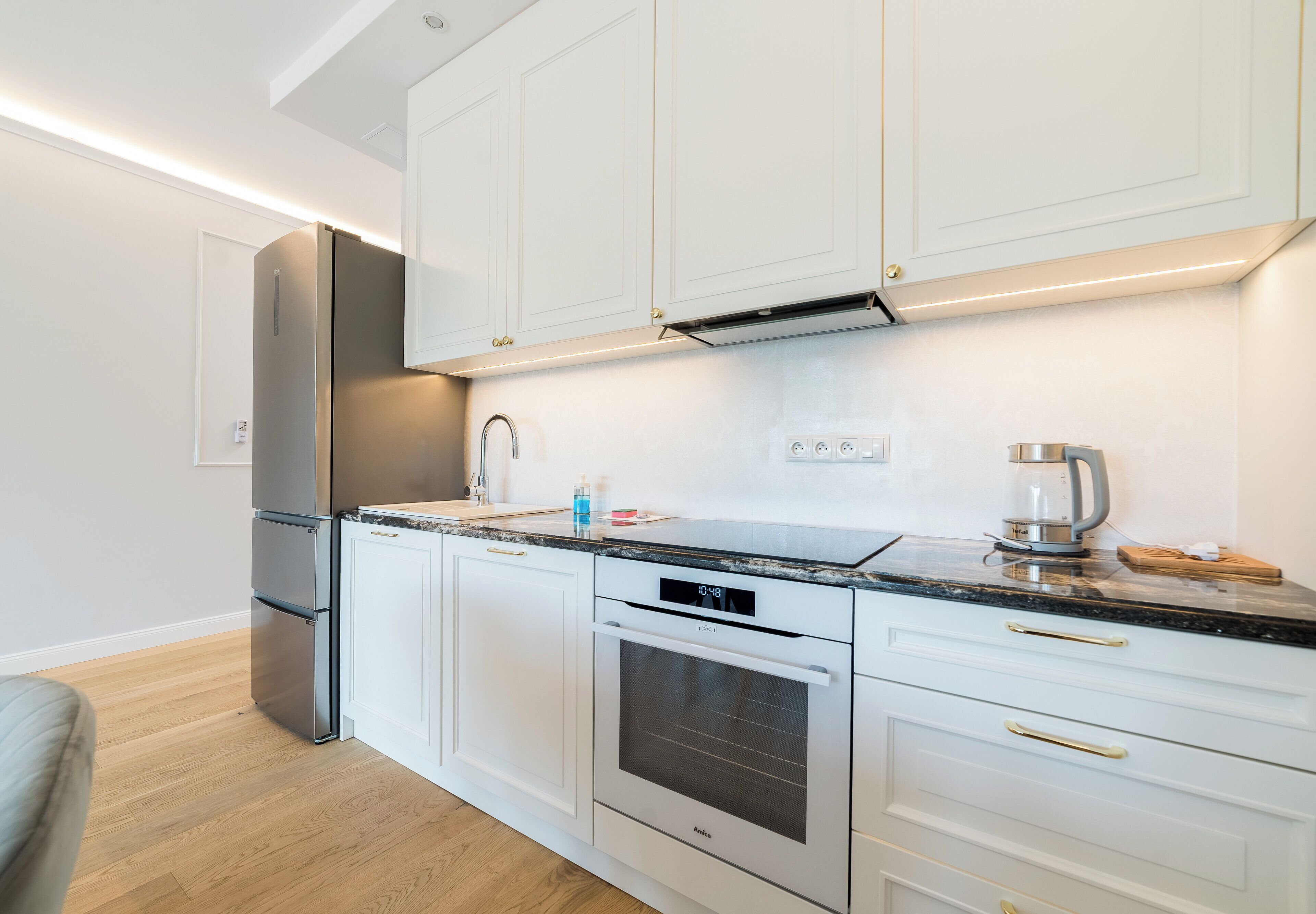 A modern kitchen with white cabinets, stainless steel appliances, and a marble countertop.