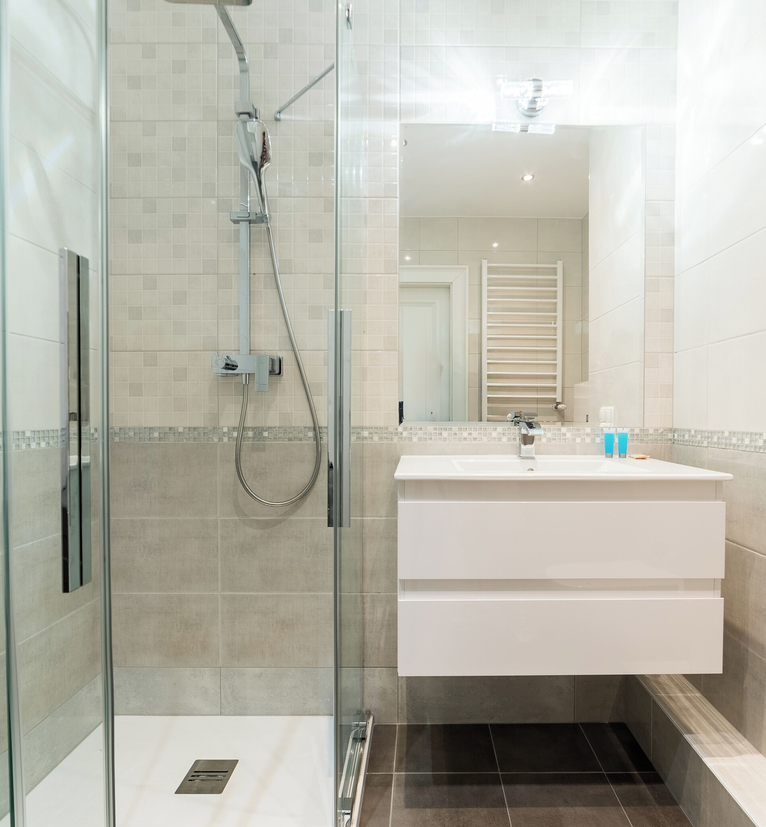 A modern bathroom with a glass-enclosed shower, a white vanity with a mirror, and a tiled floor.