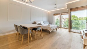 A modern bedroom with a bed, bedside table, and a view of greenery through large windows. - Warta River Chic Studio (Poznań)