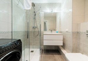A modern bathroom with a glass-enclosed shower, a built-in washing machine, a white vanity with a mirror, and a toilet. - Warta River Chic Studio (Poznań)