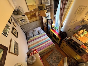 Une chambre Ă coucher avec un lit, un ventilateur de plafond, une commode et une fenĂȘtre avec des rideaux.