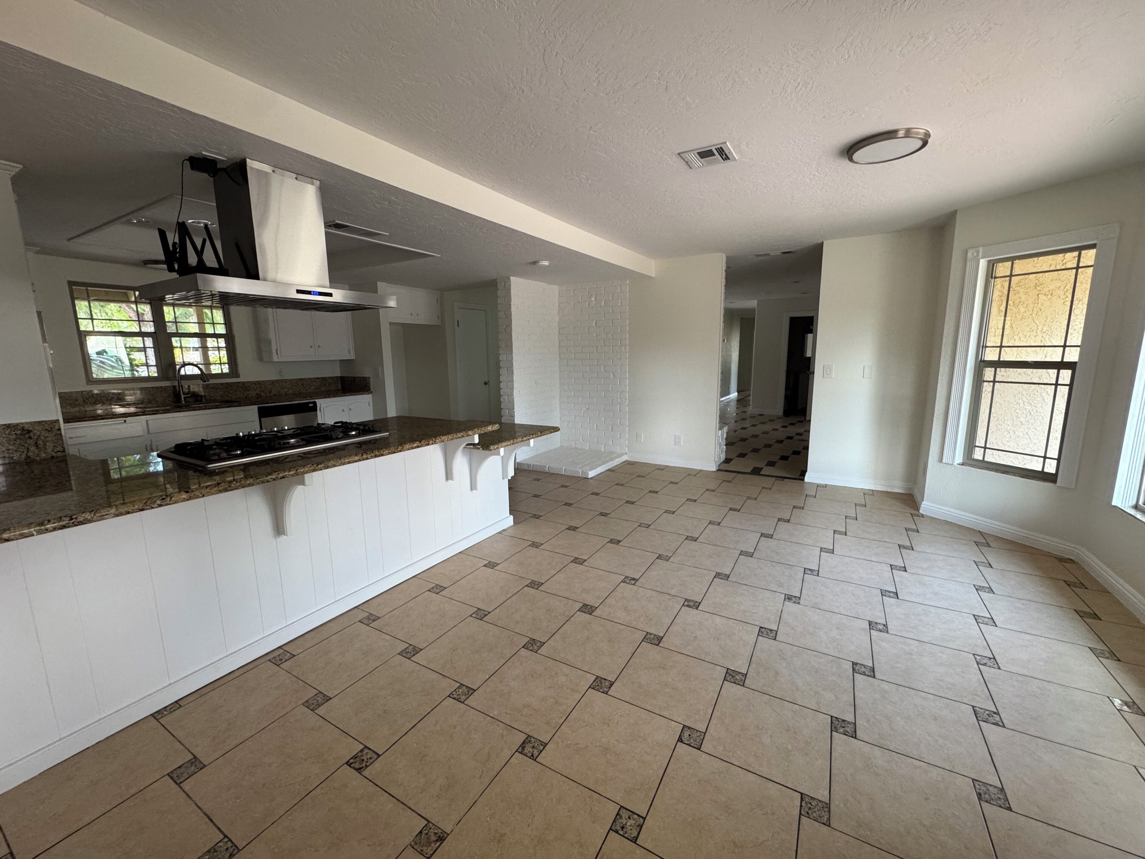 A spacious kitchen with a granite countertop, white cabinetry, and a herringbone-patterned floor.