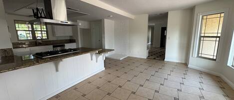 A spacious kitchen with a granite countertop, white cabinetry, and a herringbone-patterned floor.