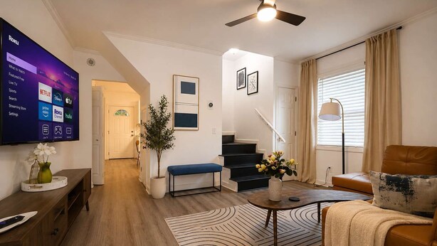 A modern living room with a flat-screen TV, a bench, a coffee table, and a staircase leading to another level. - West Midtown | Hot Tub • Fire Pit • Parking (Atlanta)