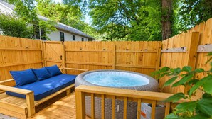 A hot tub with a wooden deck, a blue cushioned seating area, and a wooden fence. - West Midtown | Hot Tub • Fire Pit • Parking (Atlanta)