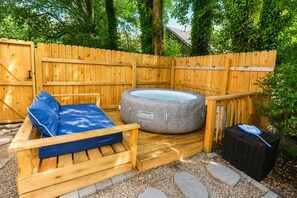 Une terrasse en bois avec un canapé d’extérieur bleu, un jacuzzi gonflable rond de la marque Coleman et une poubelle noire.