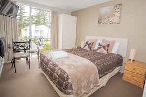 A bedroom with a bed, a chair, a bedside table, a lamp, and a window with curtains.