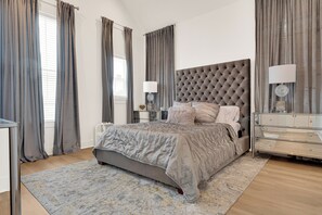 A bedroom with a tufted headboard, a bed with grey bedding, a bedside table with a lamp, and a nightstand with a lamp. - Wonderful 3-bedroom house with AC in vibrant  Houston — Minutes from Everything (Houston)