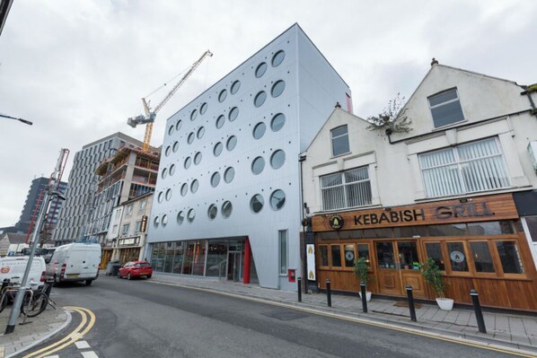 A modern building with circular windows, a kebab shop, and a construction crane in the background. - Student Only Livin (Cardiff)