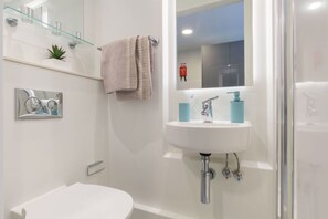 A modern bathroom with a white sink, a glass shelf with toiletries, a towel, and a mirror. - Student Only Livin (Cardiff)