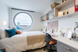 A bedroom with a round window, a bed, a desk, and shelves with various items. - Student Only Livin (Cardiff)
