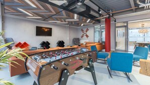 A modern indoor space with a foosball table, sofas, and a TV mounted on the wall. - Student Only Livin (Cardiff)