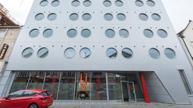 A modern building with a grid of circular windows and a prominent entrance with a red pillar. - Student Only Livin (Cardiff)