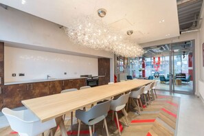 A modern kitchen with a long wooden table and chairs, a hanging light fixture, and a view into the dining area. - Student Only Livin (Cardiff)