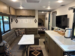 Interni di un camper compatto con angolo cottura, zona salotto e un piccolo tavolo da pranzo.