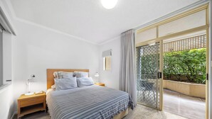 A bedroom with a bed, bedside tables, a window with curtains, and a sliding glass door leading to an outdoor area. - 1 Brm, Air Con, Parking, Wifi, Walk to City (Kangaroo Point)
