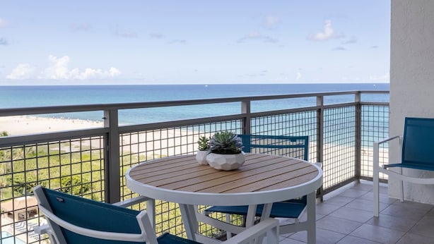 A balcony with a view of the beach, a round wooden table, and two chairs. - Thanksgiving in Florida! 2 Bedroom Ocean View Villa - Marriott's Oceana Palms (Riviera Beach)