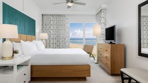 A hotel room with a bed, a TV, a desk, a chair, and a view of the beach. - Thanksgiving in Florida! 2 Bedroom Ocean View Villa - Marriott's Oceana Palms (Riviera Beach)