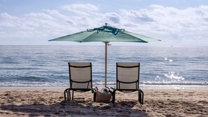 A beach with two chairs under a green umbrella, a beach chair, and a basket of items on the sand. - Thanksgiving in Florida! 2 Bedroom Ocean View Villa - Marriott's Oceana Palms (Riviera Beach)