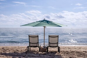 A beach with two chairs under a green umbrella, a beach chair, and a basket of items on the sand. - Thanksgiving in Florida! 2 Bedroom Ocean View Villa - Marriott's Oceana Palms (Riviera Beach)